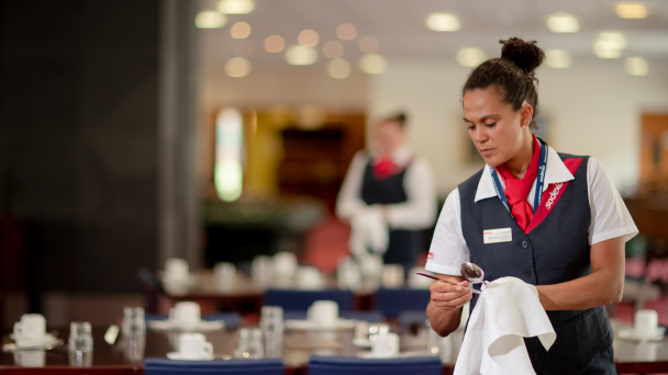 A woman in a uniform holding a napkin organising a table
