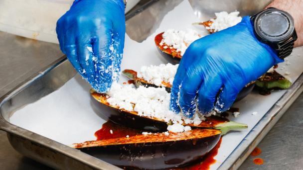A person wearing blue gloves is carefully preparing food in a kitchen