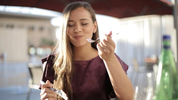 A woman enjoying a meal at a restaurant, smiling as she takes a bite of food