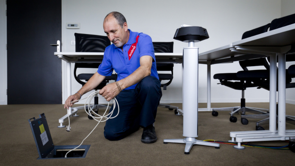 A man kneeling, attaching a cord to a desk