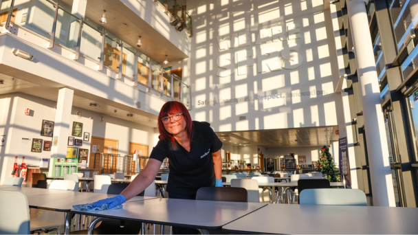 A woman smiling and wiping a table in a well-lit dining area
