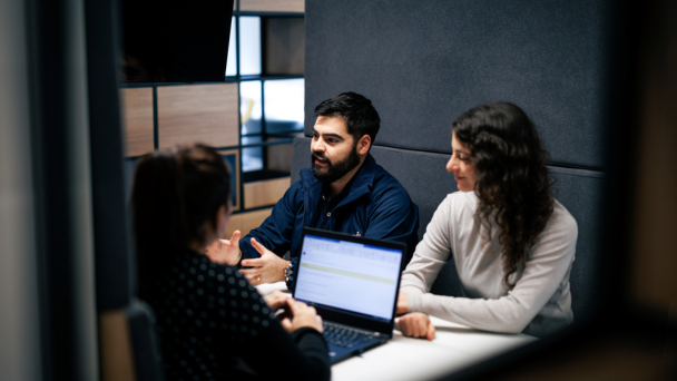 Three people sitting at a table, engrossed in their work on laptops