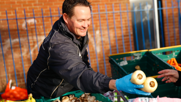 A man smiling, handing out vegtables