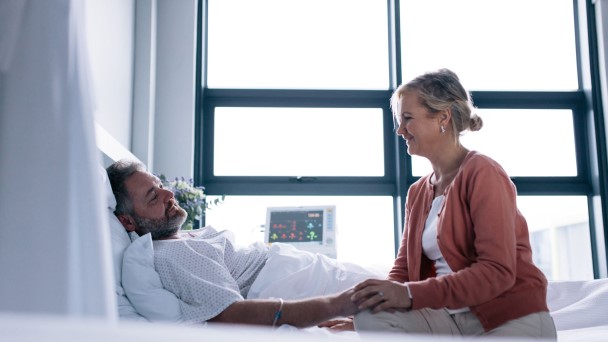 A couple seated on a hospital bed, showing support and care for each other during a difficult time