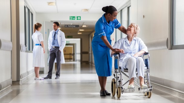 Nurse assisting elderly woman in wheelchair in hospital hallway
