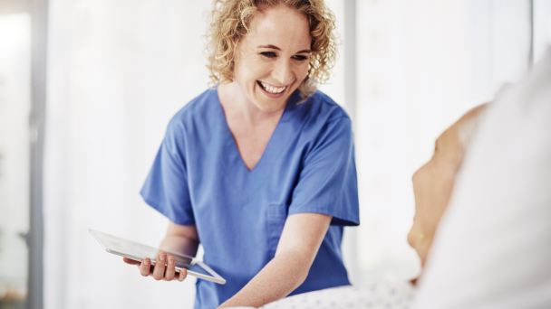 A nurse smiling at a patient while holding a tablet.