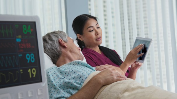 Female nurse is holding a tablet and showing a patient the screen