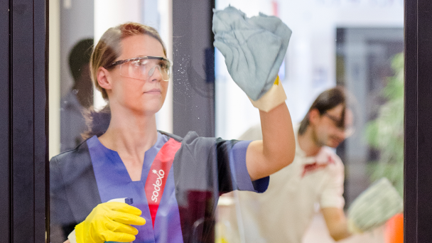 A woman in a blue uniform cleaning a window with a squeegee
