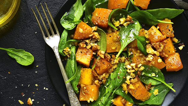 A plate of spinach and squash salad with a fork