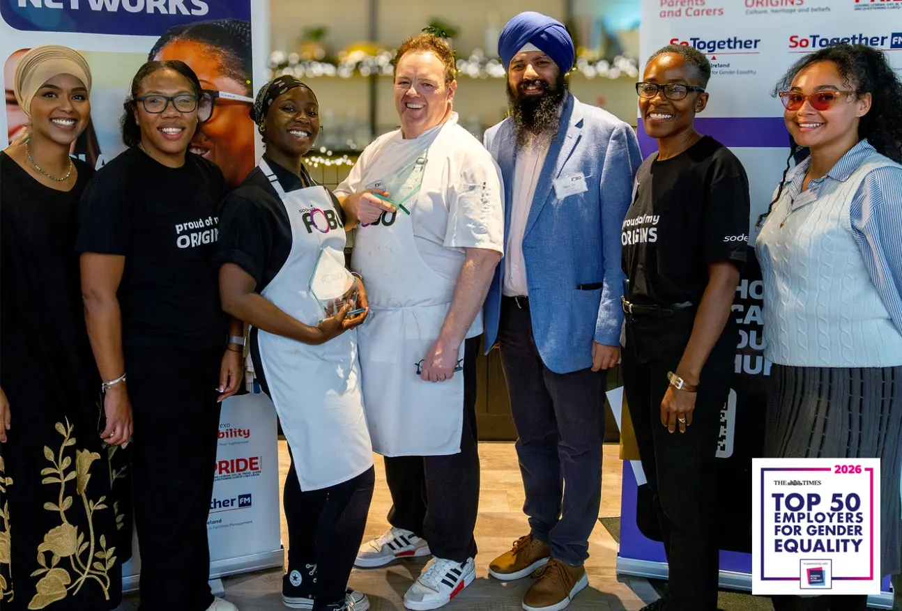 A diverse group of Sodexo team members standing at an event booth, including individuals in chef attire and branded 