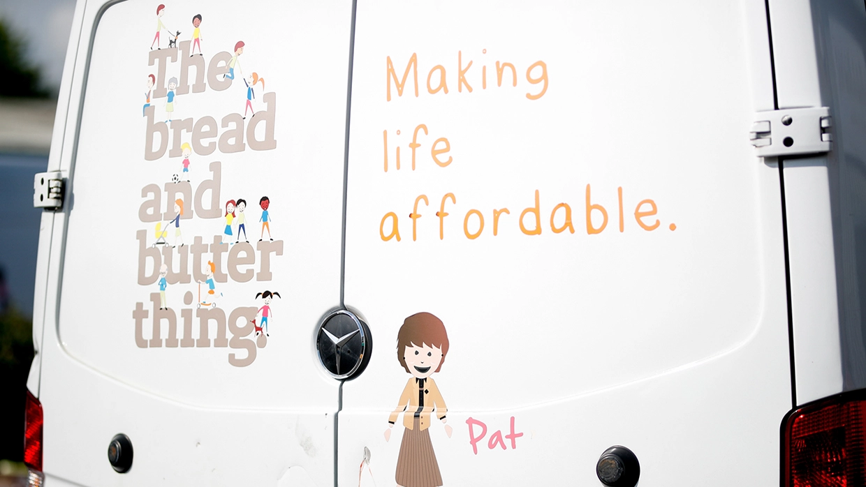 White delivery van featuring illustrated people and the text the bread and butter thing alongside the slogan Making life affordable. A cartoon-style character labeled Pat appears on the back doors