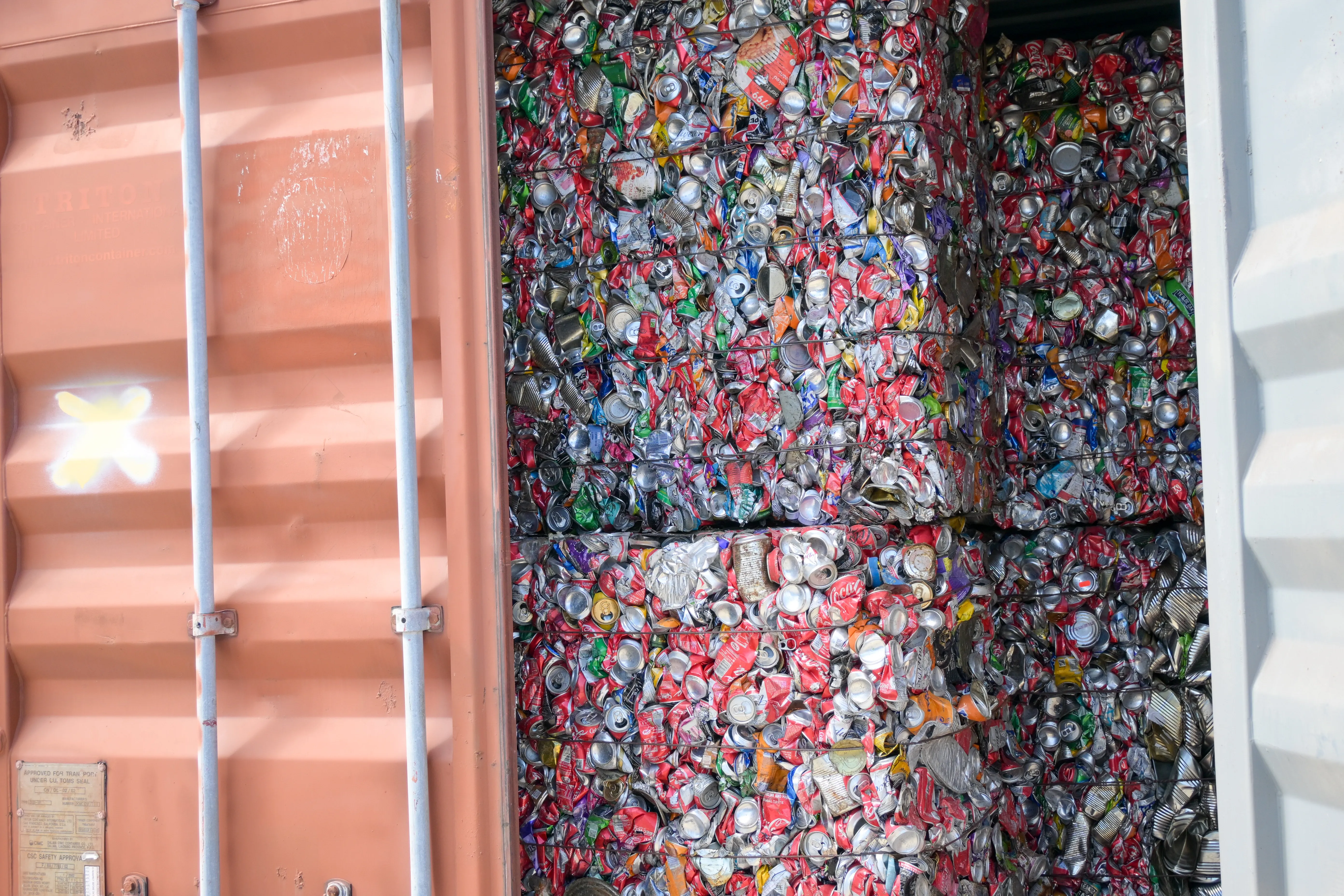 Compacted bales of crushed aluminium drinks cans stacked inside a shipping container for recycling.