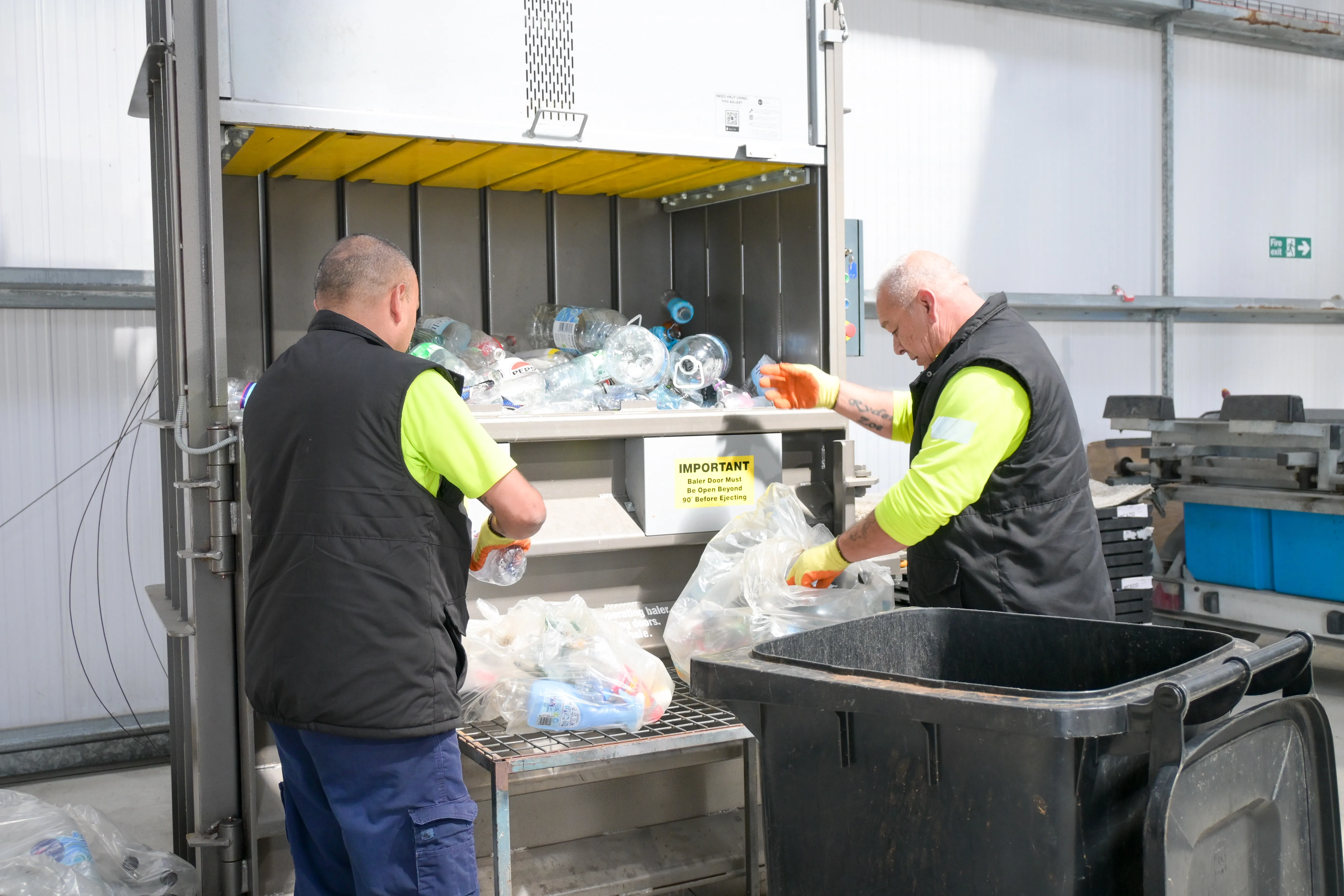 Workers sorting plastic bottles into a recycling compactor at a materials recovery facility.