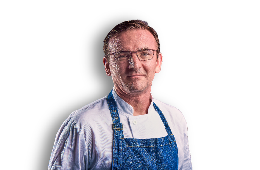 person in a chef’s apron posing for a professional staff portrait against a plain background.