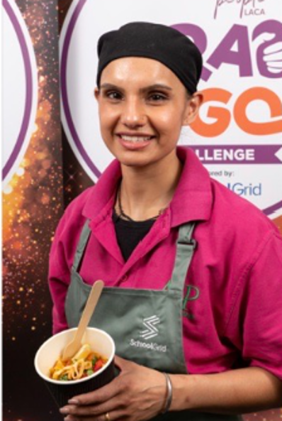 Person in a chef’s uniform holding a plated dish at a food service event.