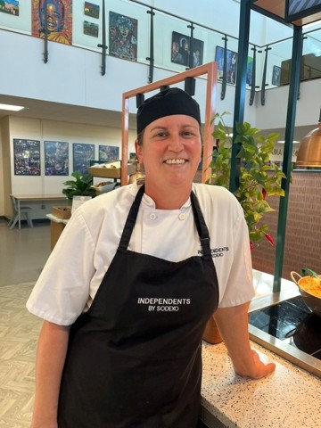 Person wearing a chef’s uniform and apron outdoors beside a catering or hospitality setting.