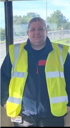 Sodexo colleague wearing a high-visibility vest standing indoors near large windows.