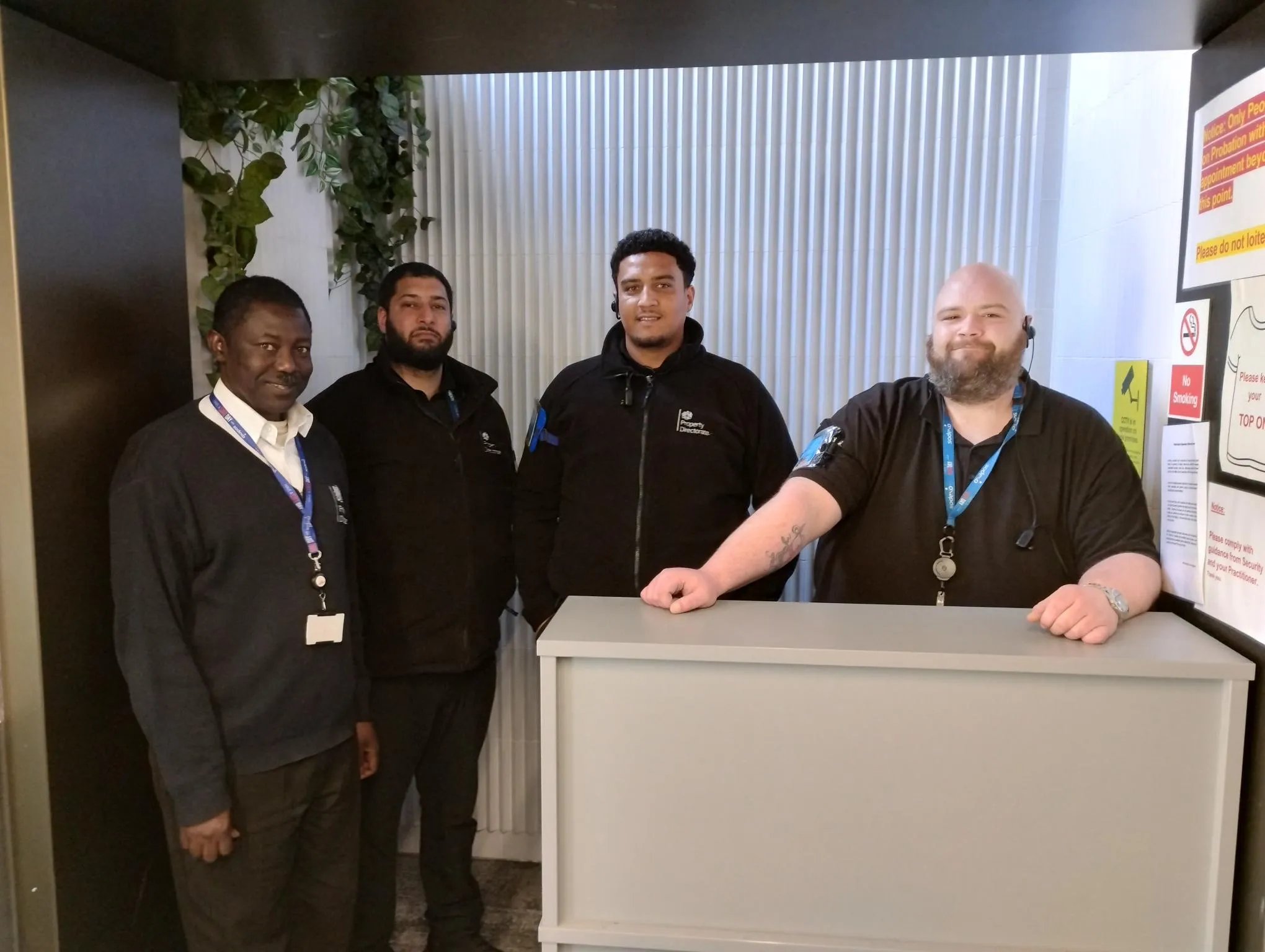 Four Sodexo property services colleagues standing behind a reception desk inside a workplace environment.