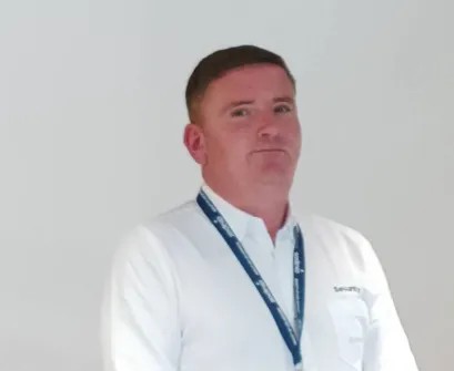 Sodexo security colleague wearing a white uniform shirt and staff lanyard standing beside an indoor staircase.