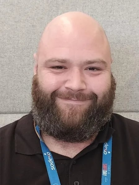 Headshot of a Sodexo colleague wearing a black polo shirt and staff lanyard against a neutral background.