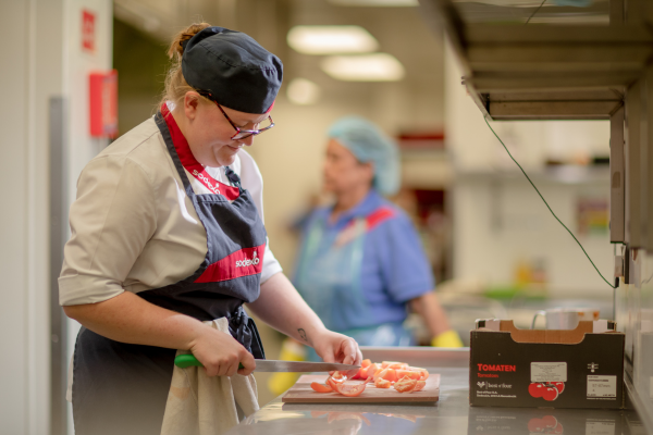 A woman in uniform cutting tomatoes on a counter.