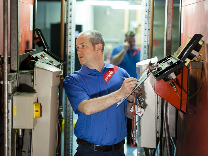 A man wearing sodexo blue uniform shirt writing on a clipboard and inspecting