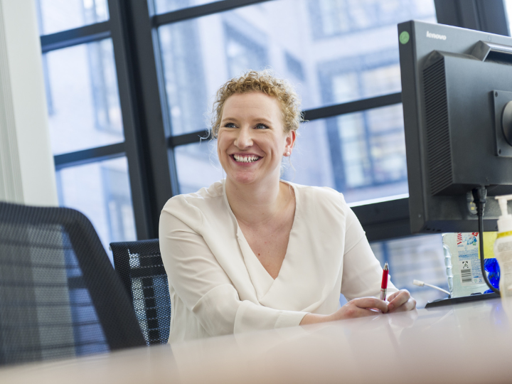 A woman smiling in front of a computer screen, looking happy and engaged
