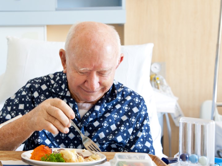 An elderly male patient is eating in his hospital bed