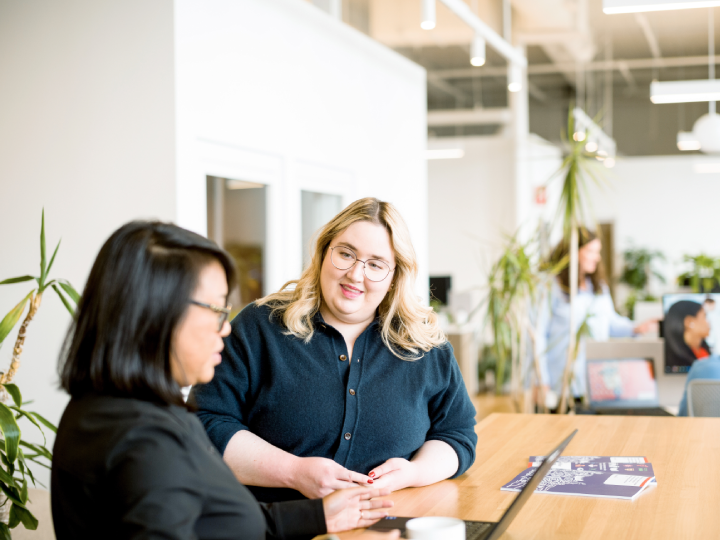 Two women sitting at a table in an office, engaged in a conversation