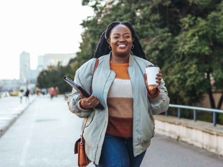 A happy African American woman walking down the street with a coffee in hand