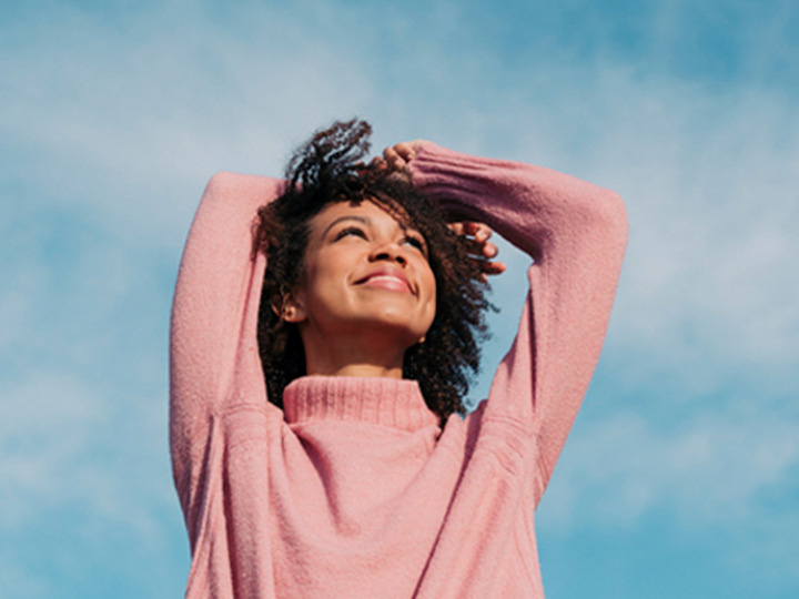 A woman in a pink sweater gazes upwards at the sky