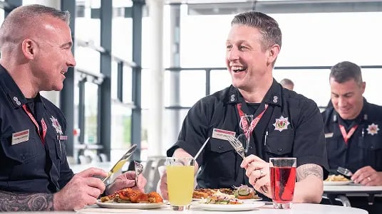 Uniformed service staff seated at a cafeteria table eating meals together in a bright, modern dining area