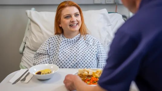 Patient receiving a meal service at the bedside in a hospital ward.