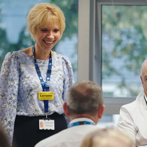 Healthcare employee leading a discussion with colleagues during a meeting in a hospital setting.