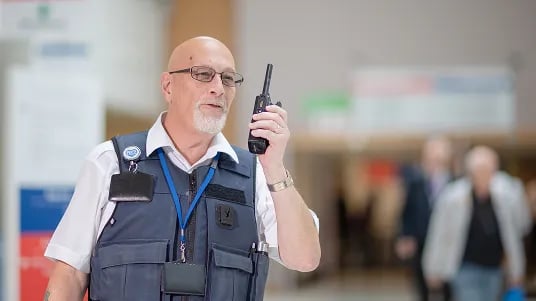 Security officer using a two-way radio while monitoring activity in a healthcare facility.
