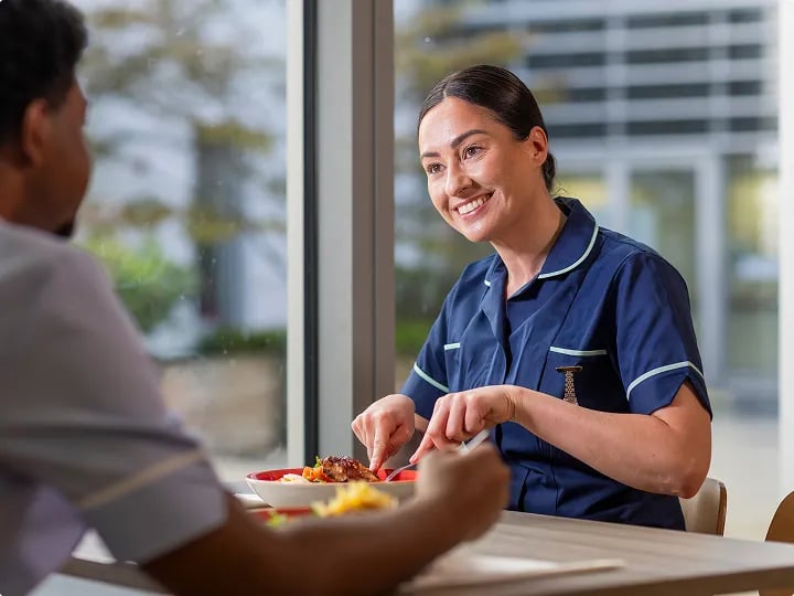 Healthcare staff member sharing a meal with a colleague in a hospital dining area.