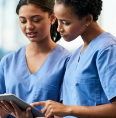 Two female nurses are looking at a tablet that one of them is holding