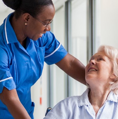 A nurse is smiling and looking down at a female patient in a wheelchair