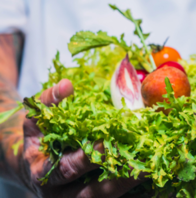 An image of a hand holding a handful of greens and tomatoes on top
