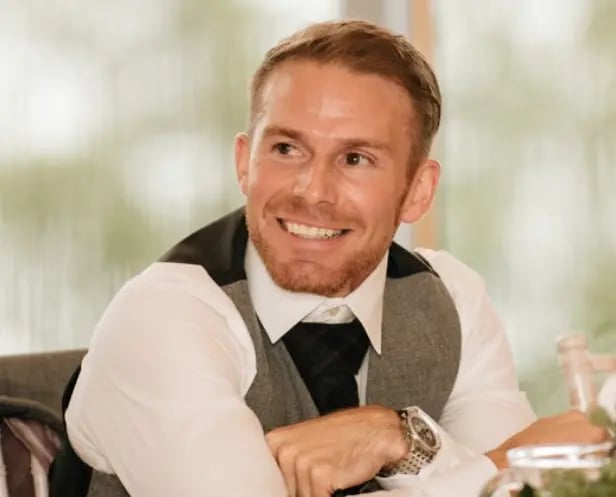 Person in a white shirt, tie, and vest sitting at a table, looking to the side.