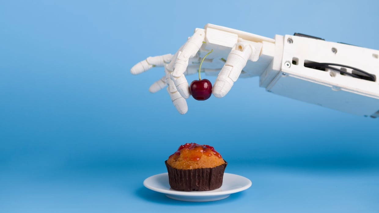main de robot qui pose une cerise sur un gâteau