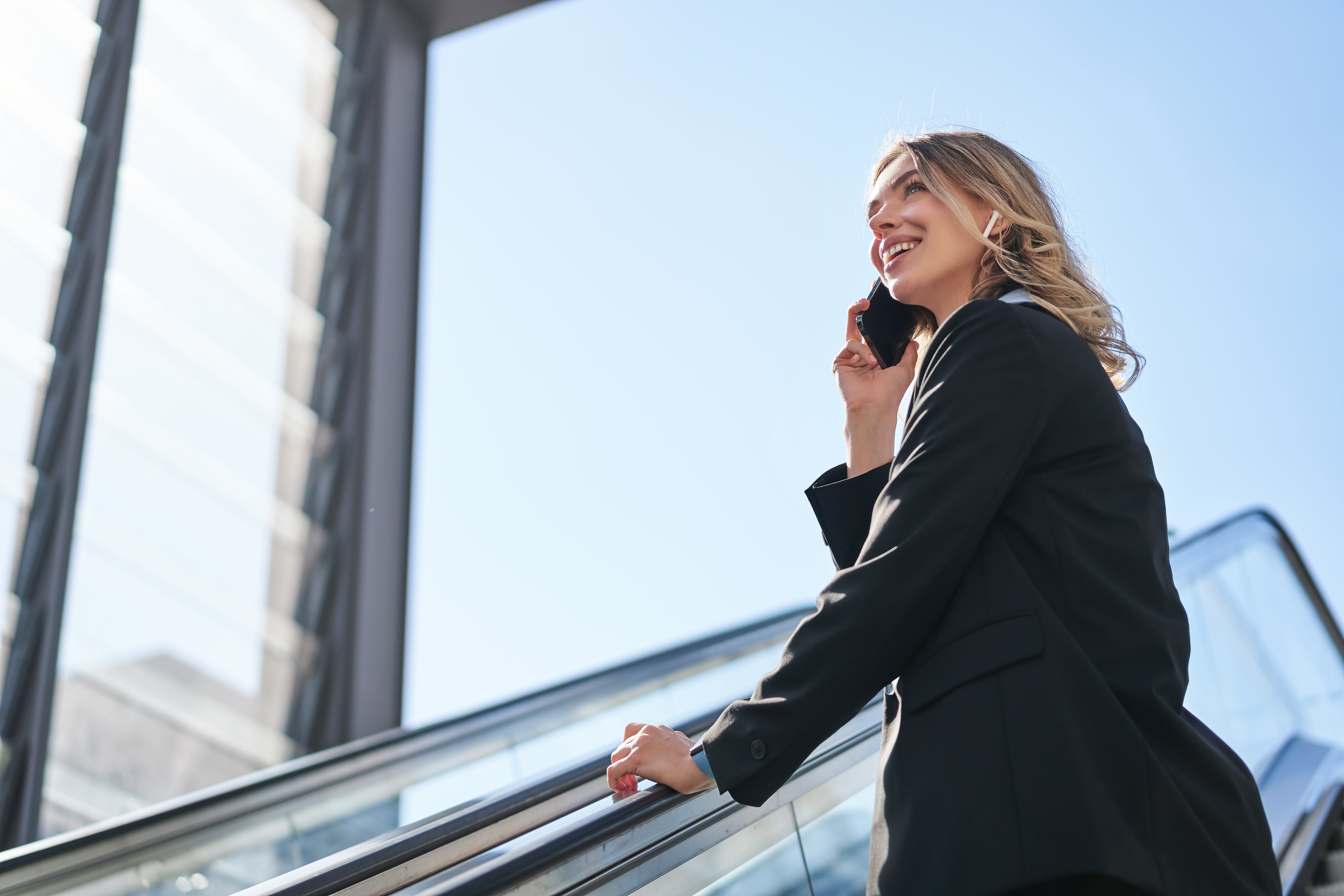 portrait-businesswoman-black-suit-going-up-escalator-talking-mobile-phone-saleswoman-wal