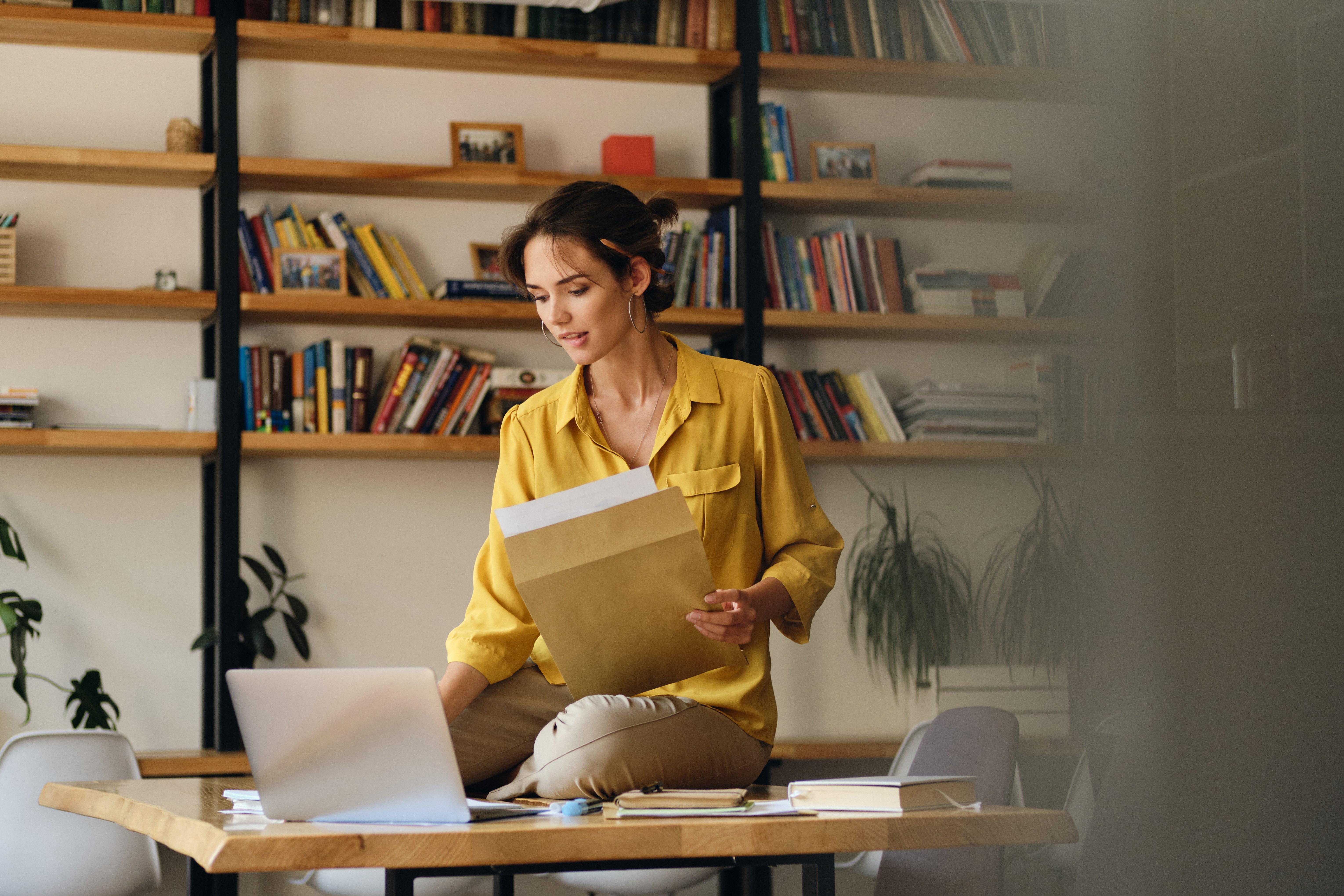 young-beautiful-woman-yellow-shirt-sitting-desk-with-laptop-papers-while-dreamily-working-modern-office