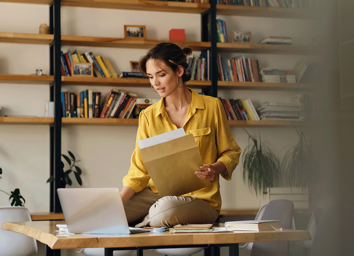 youngbeautifulwomanyellowshirtsittingdeskwithlaptoppaperswhiledreamilyworkingmodernoffice