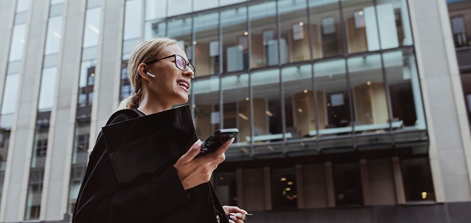 Dame foran kontorbygg med mobiltelefon i hånden.