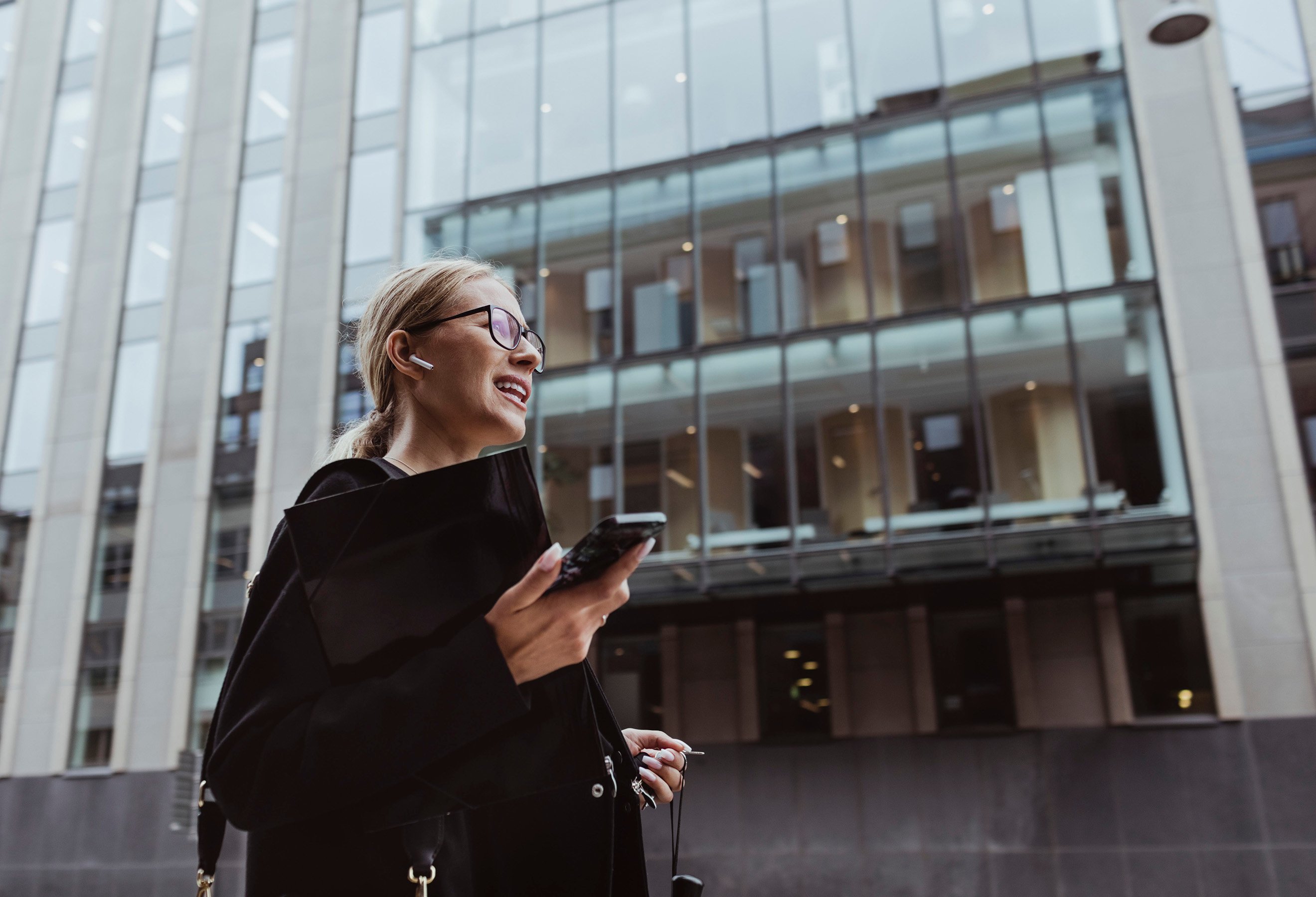 mobilbank bedrift: Dame foran kontorbygg med mobiltelefon i hånden.