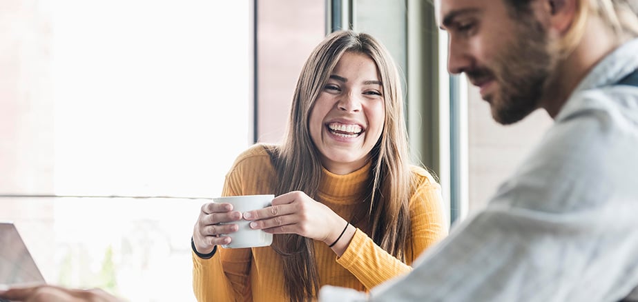 Bankgaranti: Dame med kaffekopp ler mot mann foran laptop.