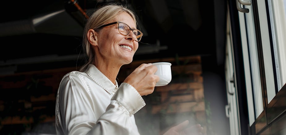 Lån: Dame med kaffekopp som ser ut av vinduet.