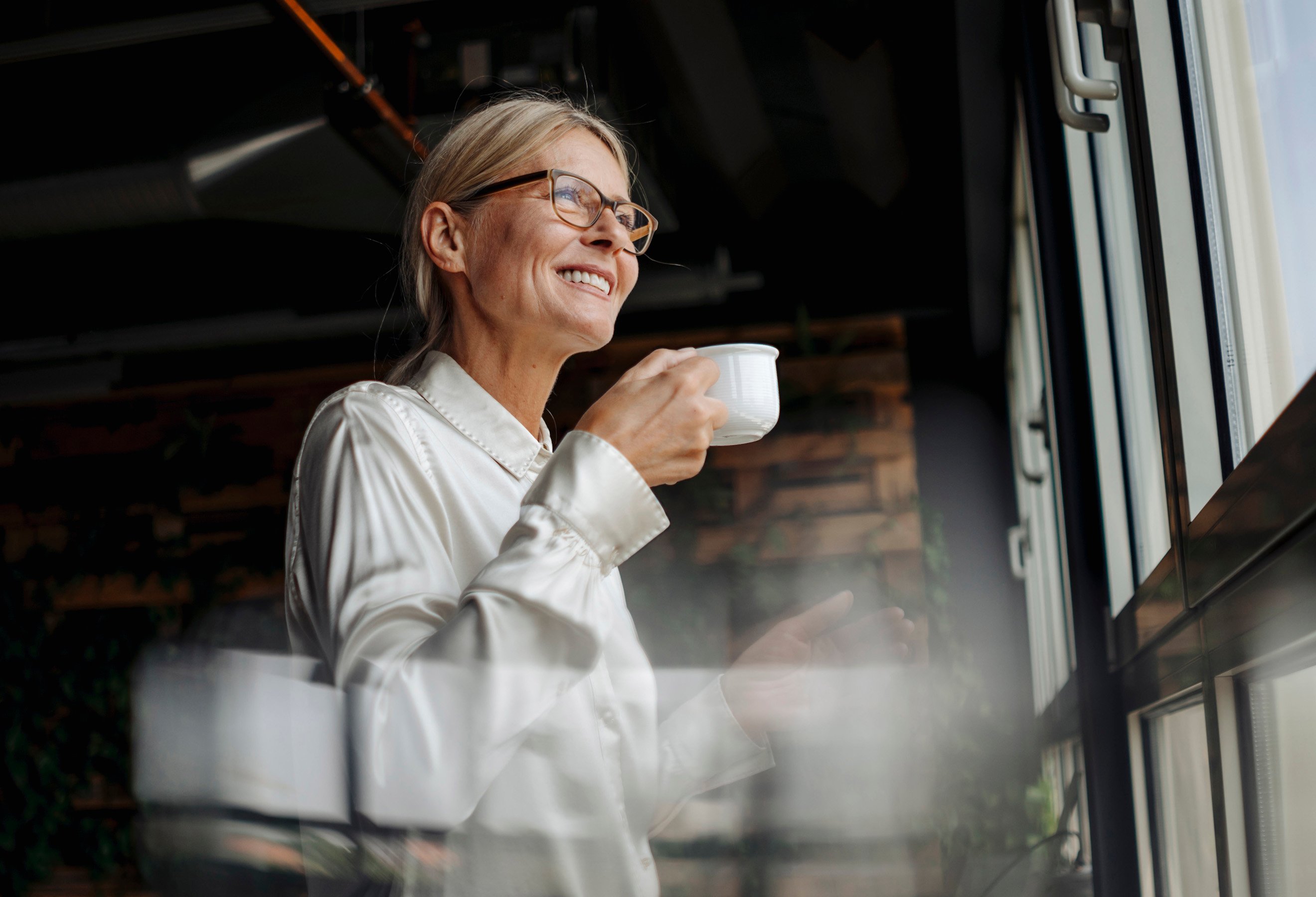 Lån: Dame med kaffekopp som ser ut av vinduet.