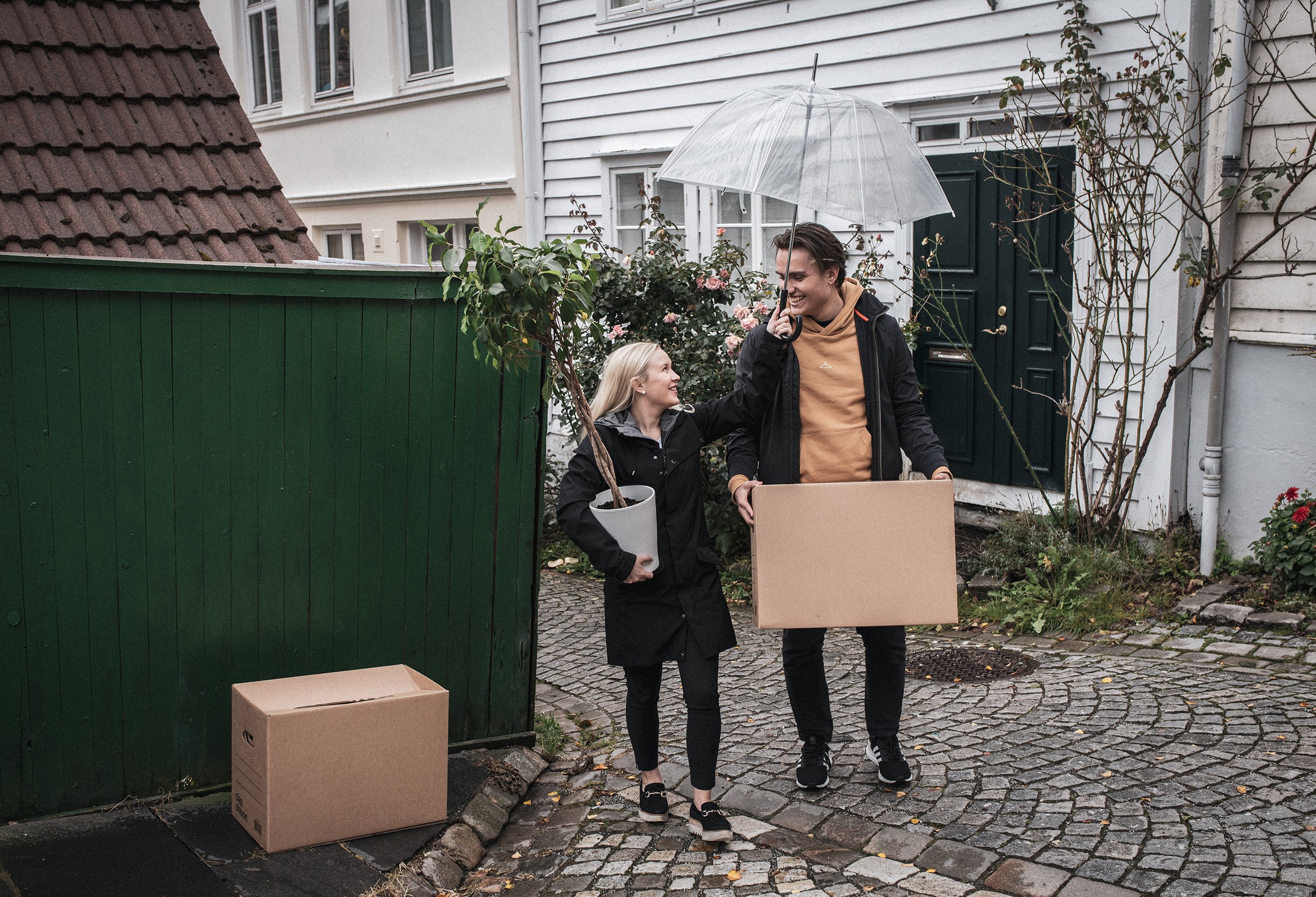 Ungt par bærer flyttekasser og plante i et smau.